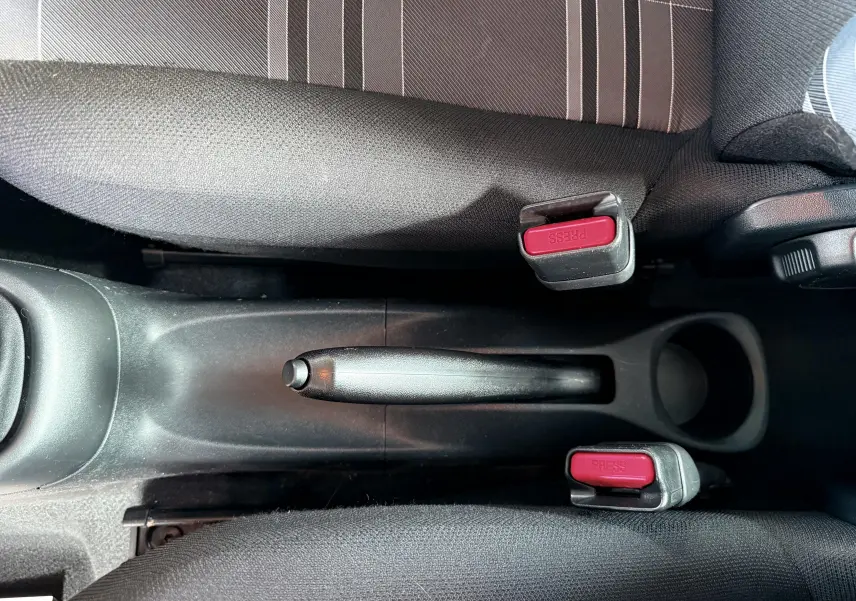 Vue plongeante sur le frein à main noir entre les sièges avant en tissu gris foncé d'une Peugeot 108 noire.