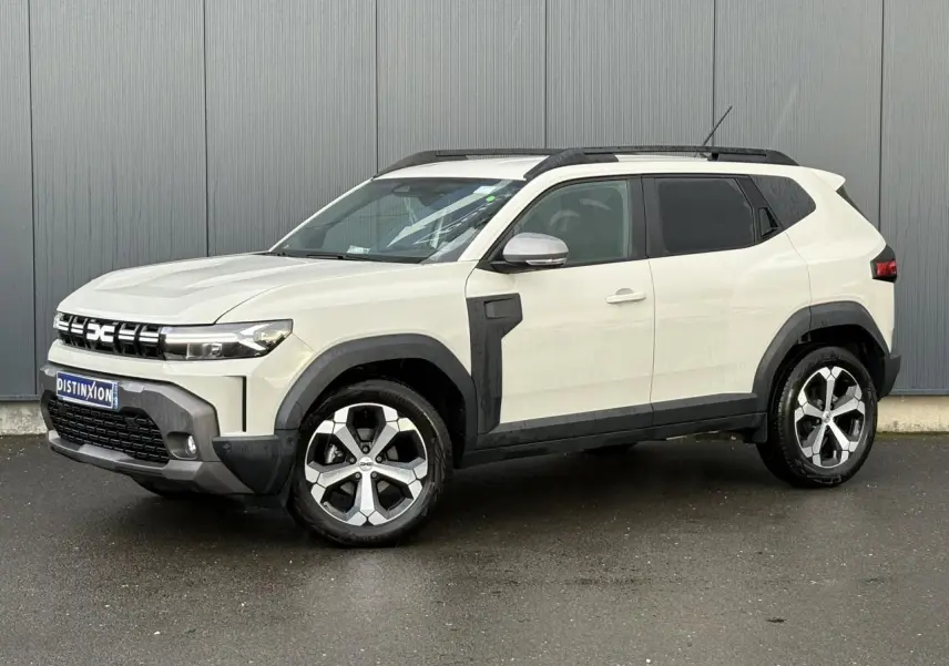 Vue 3/4 avant droit du Dacia Duster 2024 beige Sandstone avec barres de toit noires et jantes alliage distinctives.