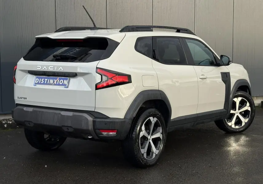 Vue 3/4 arrière droite du Dacia Duster beige Sandstone 2024 avec barres de toit noires et jantes alliage.