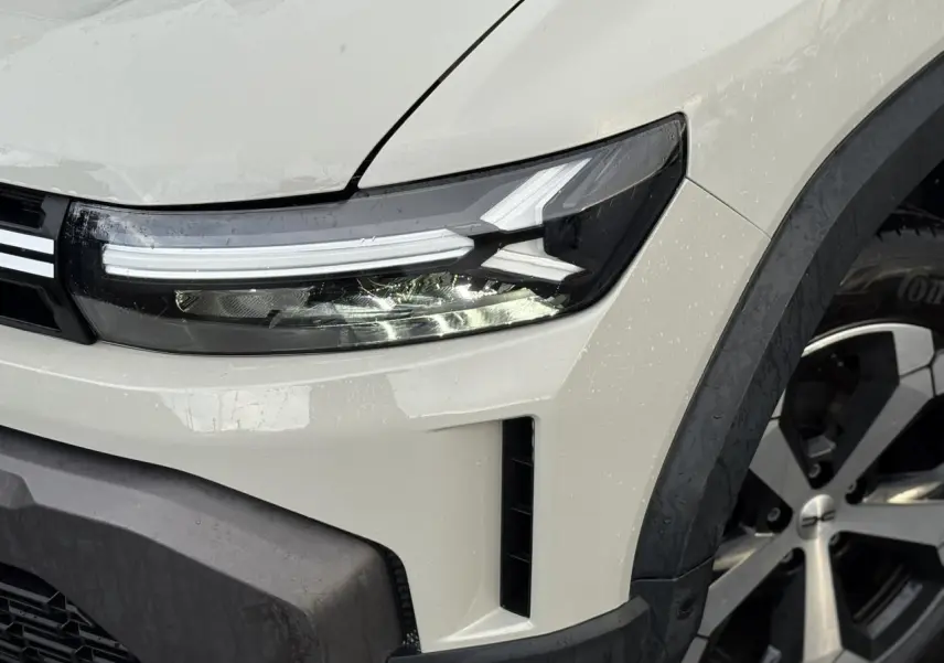 Gros plan sur l'avant droit du Dacia Duster 2024 beige Sandstone, mettant en valeur le phare LED et la jante alliage.