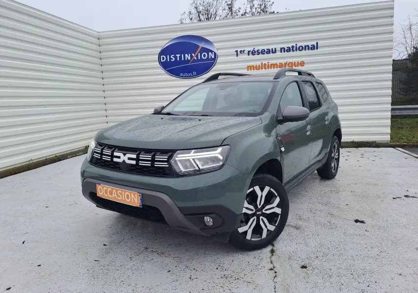 Vue 3/4 avant droite d'un Dacia Duster 2023 kaki Liken avec attelage et jantes bi-ton noires et argentées.