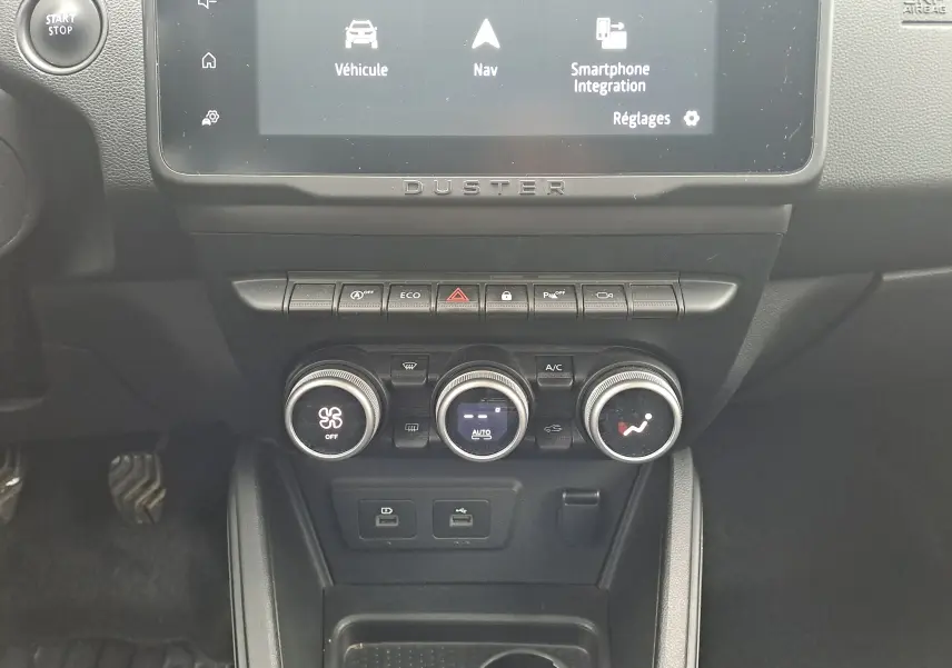 Vue rapprochée du tableau de bord noir du Dacia Duster 2023, avec commandes climatisation et écran tactile affichant la navigation.