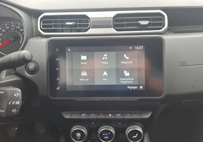 Vue rapprochée de l’écran tactile central et du tableau de bord noir du Dacia Duster 2023, avec commandes climatisation et bouton start/stop.