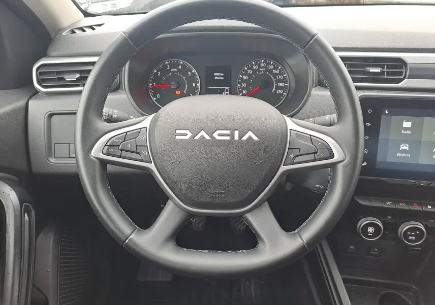 Vue centrée sur le volant noir du Dacia Duster 2023 avec tableau de bord et écran tactile en arrière-plan.