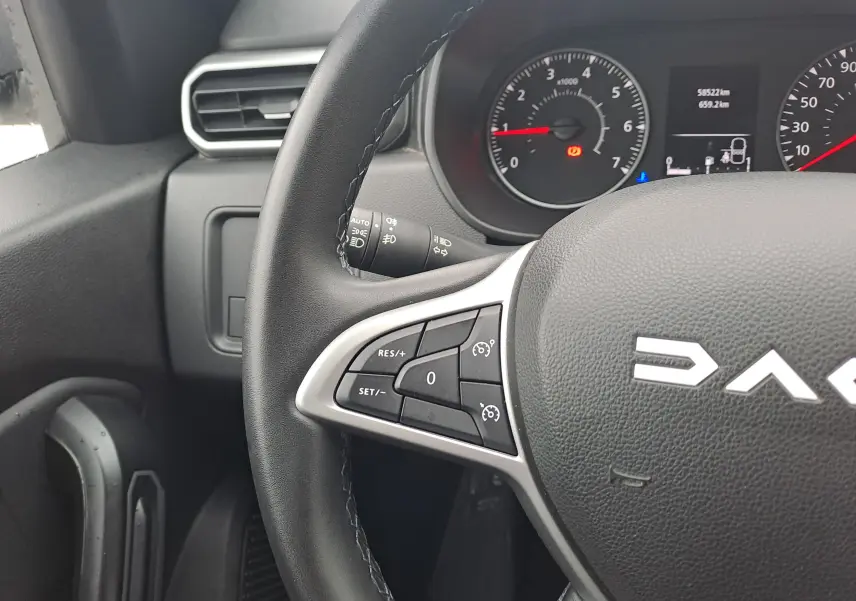 Gros plan sur le volant noir du Dacia Duster 2023, montrant les commandes de régulateur de vitesse et le tableau de bord en arrière-plan.