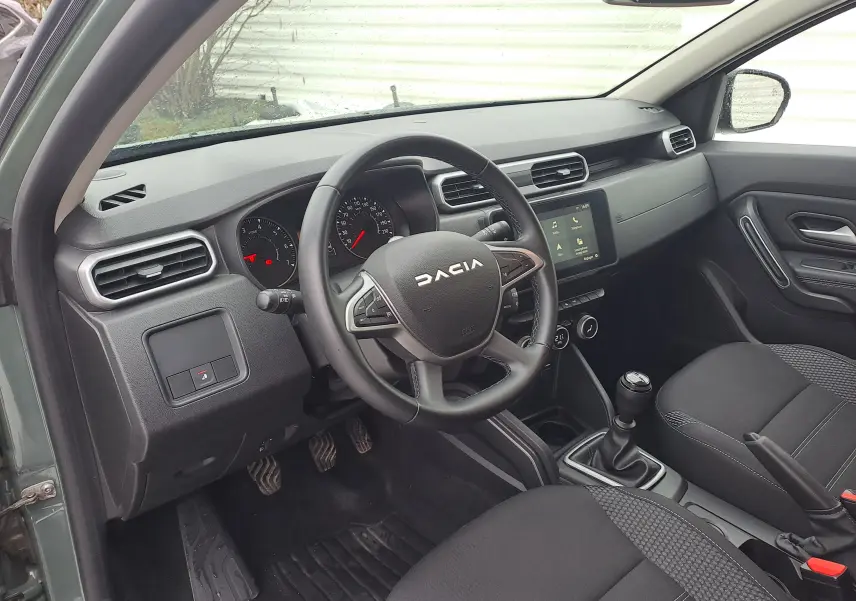 Vue intérieure côté conducteur du Dacia Duster 2023 kaki Liken, volant multifonction et boîte manuelle visibles.