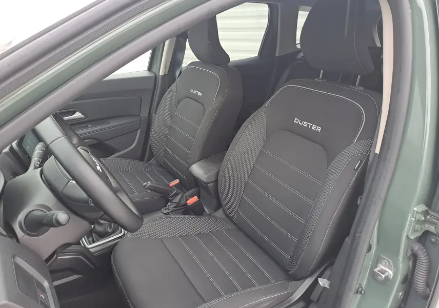 Vue intérieure côté conducteur du Dacia Duster 2023 kaki Liken, sièges noirs avec logo Duster brodé.