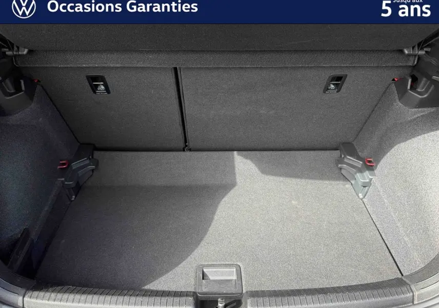 Coffre ouvert de la Volkswagen Polo rouge, vue arrière montrant l’espace de chargement vide et la moquette grise.