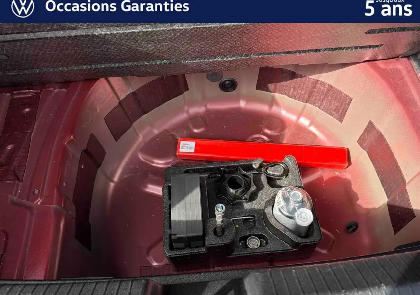 Vue rapprochée de la roue de secours rouge métallisée d’une Volkswagen Polo 2025 avec kit de réparation et triangle de signalisation.