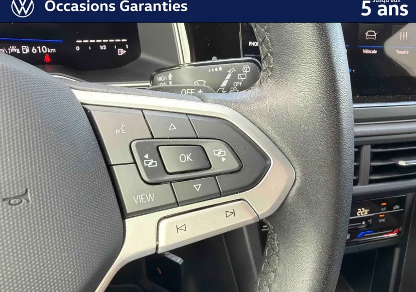 Gros plan sur les commandes multifonctions à droite du volant cuir d’une Volkswagen Polo rouge, avec tableau de bord digital en arrière-plan.