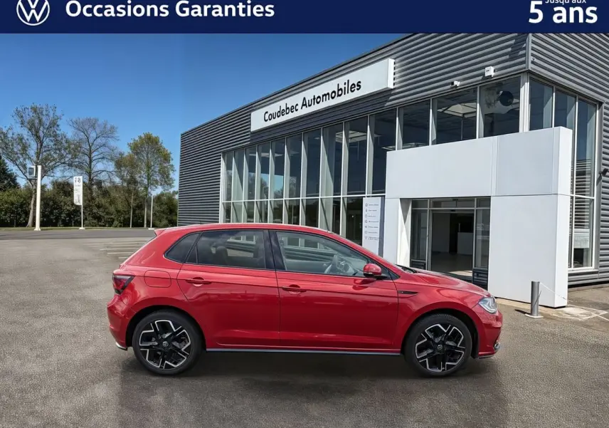 Volkswagen Polo rouge vue de profil côté gauche, garée devant un bâtiment moderne de concession.