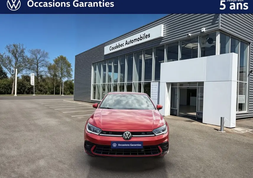 Vue avant d'une Volkswagen Polo rouge métallisée garée devant un bâtiment moderne de concession automobile.