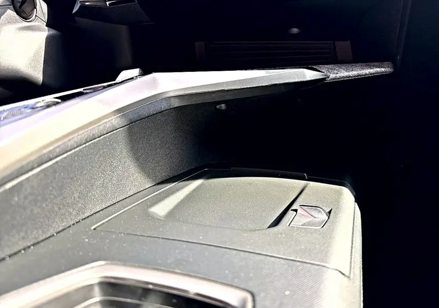 Gros plan sur la boîte à gants fermée noire du Peugeot 5008 Hybrid 145 GT e-dcs6, intérieur sombre.