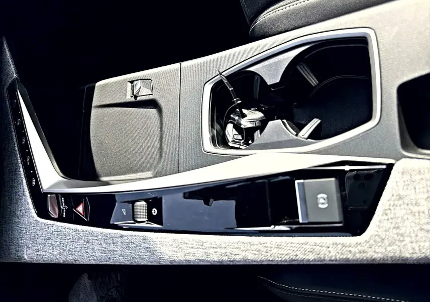 Gros plan de la console centrale intérieure du Peugeot 5008 Hybrid noir, avec porte-gobelets et commandes électroniques.