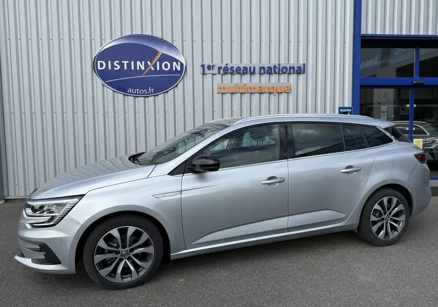 Profil droit d'une Renault Mégane Break gris Highland Metal 2024 stationnée devant un bâtiment commercial.