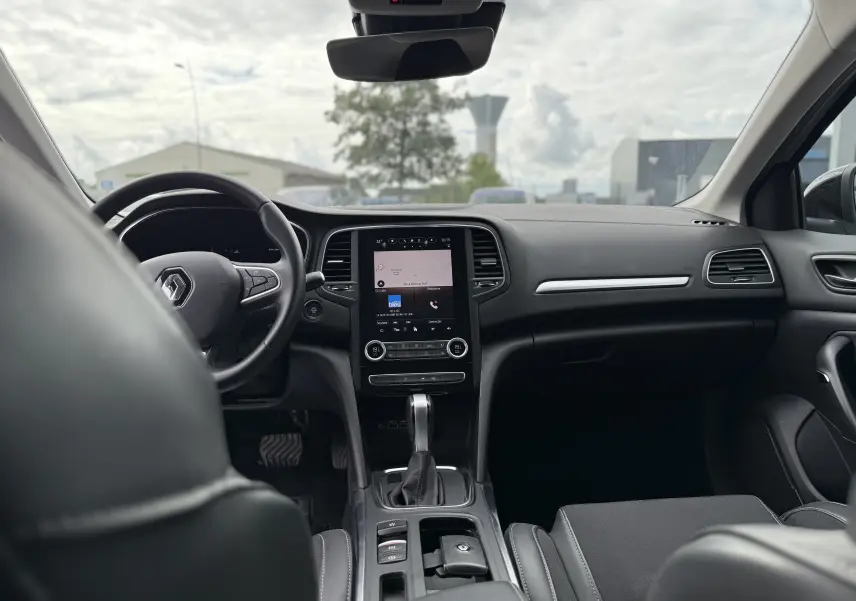 Vue intérieure avant de la Renault Mégane Break 2024, tableau de bord moderne avec écran tactile et volant multifonction noir.