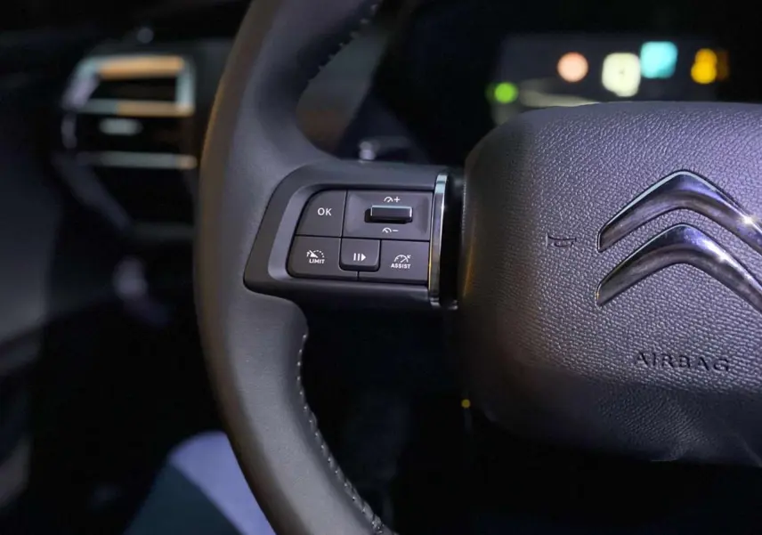 Gros plan sur le volant cuir noir du Citroën C5 X 2023 avec commandes intégrées côté gauche et logo chromé central.