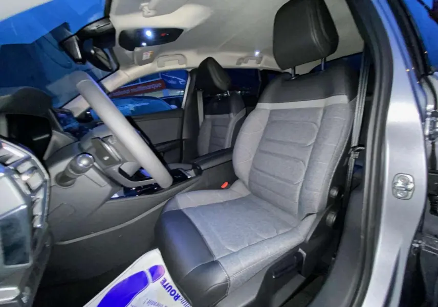 Vue intérieure côté conducteur de la Citroën C5 X 2023 gris Artense, sièges tissu gris avec appuie-tête noir.