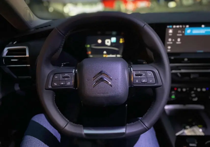 Volant en cuir noir avec commandes intégrées dans l'habitacle sombre d'une Citroën C5 X 2023, vue conducteur.