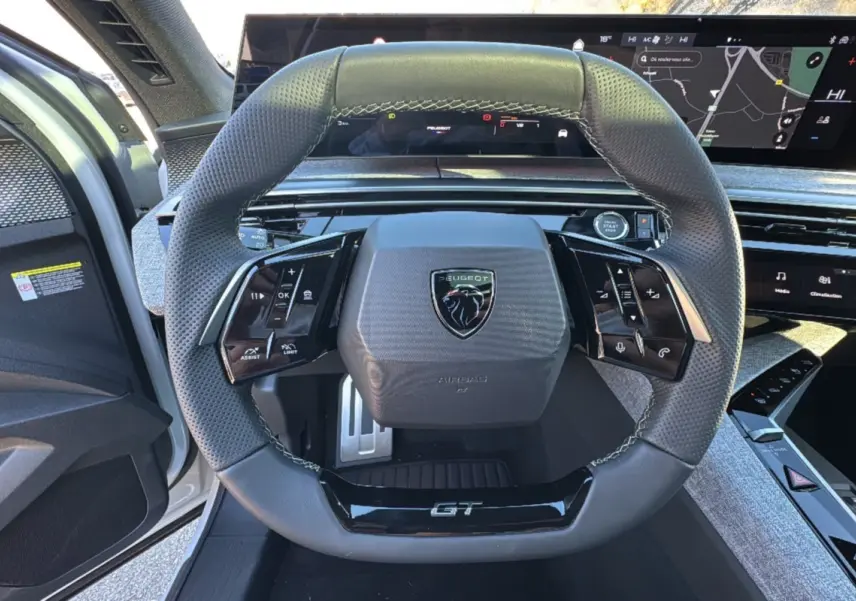 Vue centrée du volant GT noir perforé du Peugeot 3008 Hybrid 2024 avec tableau de bord numérique et portière blanche ouverte.