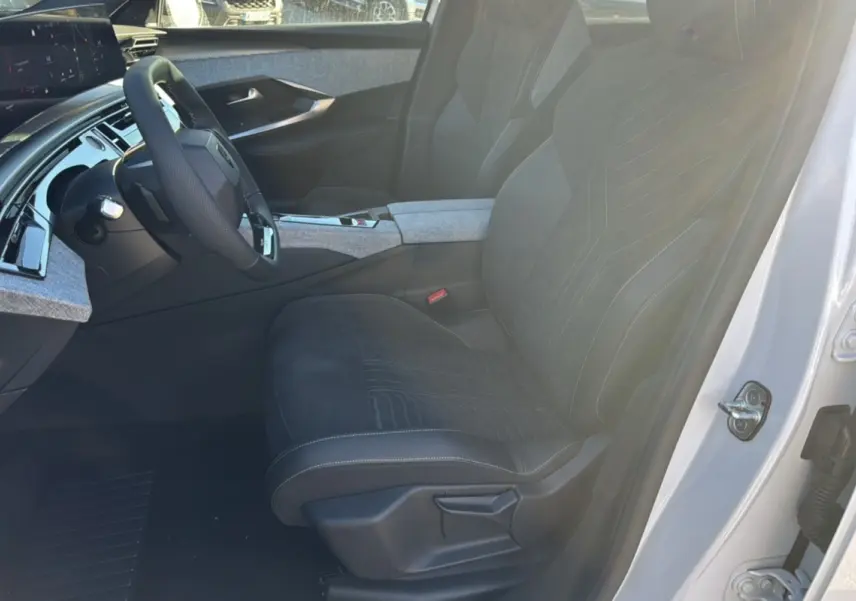 Vue intérieure côté conducteur du Peugeot 3008 Hybrid 2024 blanc okénite, avec sièges en tissu et alcantara noirs et tableau de bord moderne.