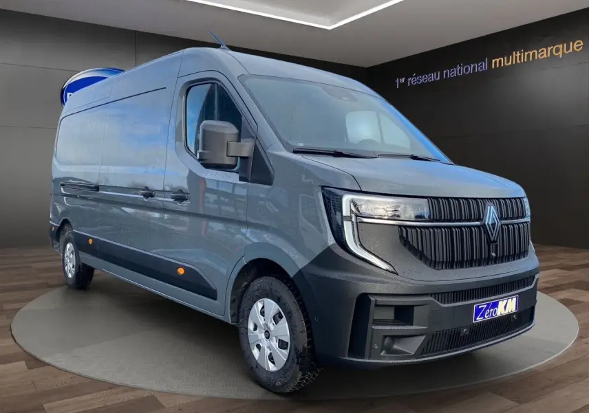 Vue 3/4 avant du Renault Master gris urbain 2025 avec calandre noire distinctive et jantes argentées, en showroom.