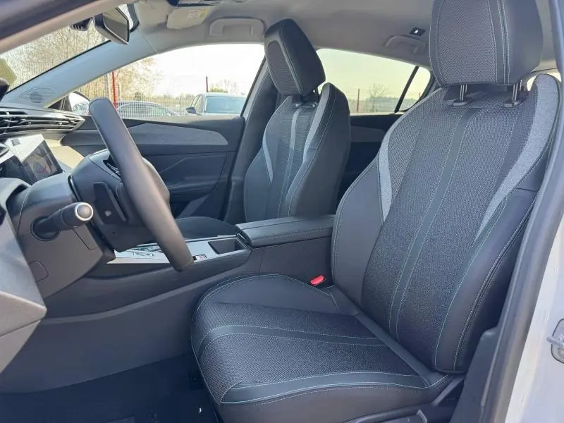 Vue intérieure côté conducteur de la Peugeot 308 2025, sièges tissu noir avec surpiqûres grises, console centrale et volant multifonction.