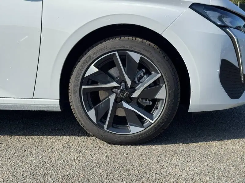 Gros plan sur la roue avant droite avec jante alu noire et grise de la Peugeot 308 blanc Okénite.