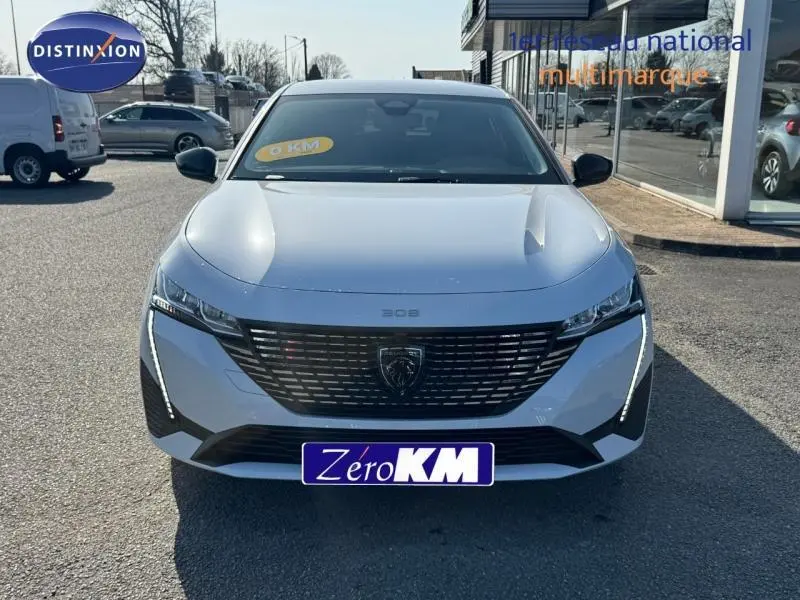 Vue avant d'une Peugeot 308 blanche Okénite avec calandre noire et feux LED verticaux allumés.