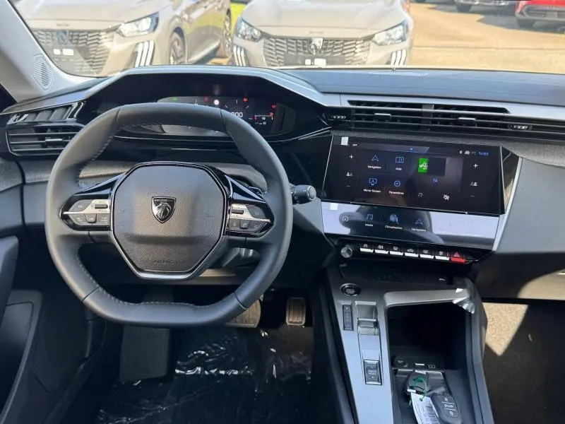 Vue intérieure avant du poste de conduite de la Peugeot 308 2025, volant multifonction et écran tactile central.