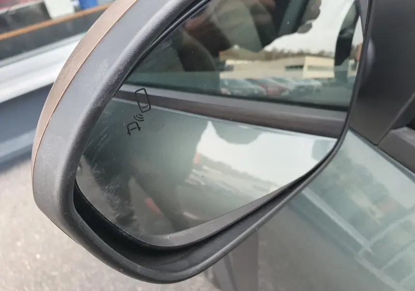 Rétroviseur côté gauche du Dacia Jogger vert cèdre 2026 avec signalisation d'alerte d'angle mort visible.