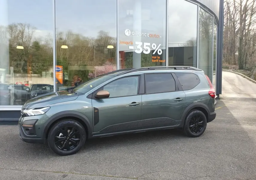 Vue de profil côté gauche d'un Dacia Jogger vert cèdre avec jantes noires et barres de toit longitudinales.