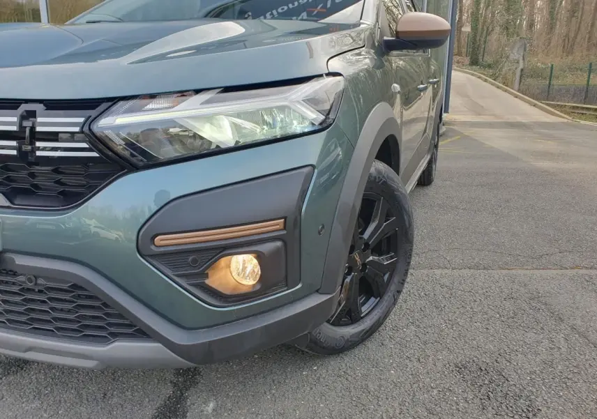 Gros plan sur l'avant droit du Dacia Jogger vert cèdre, avec phare LED et jante noire distinctive.