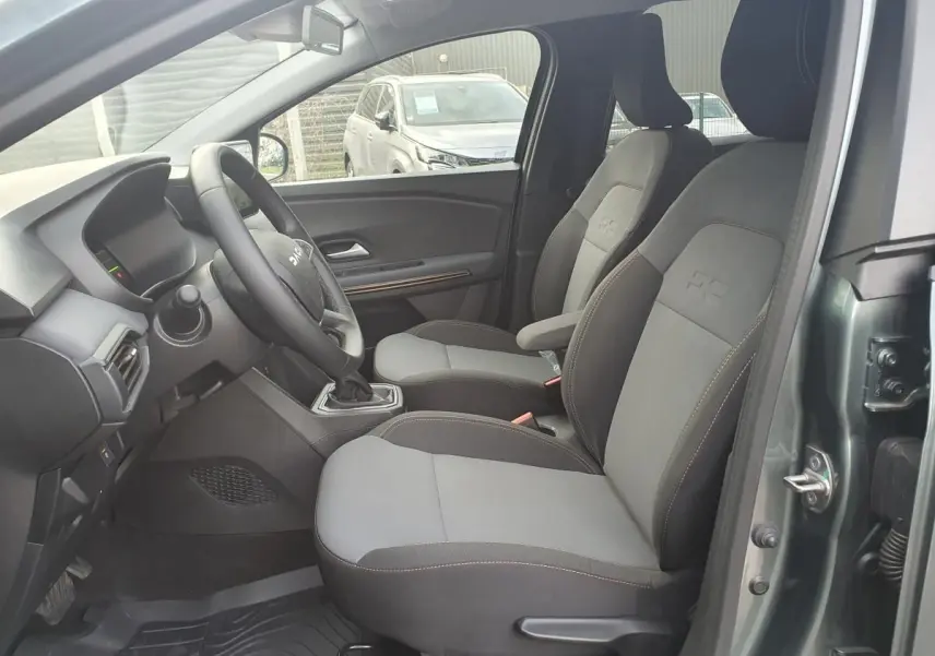 Vue intérieure côté conducteur du Dacia Jogger vert cèdre, montrant les sièges avant gris et noirs avec surpiqûres.