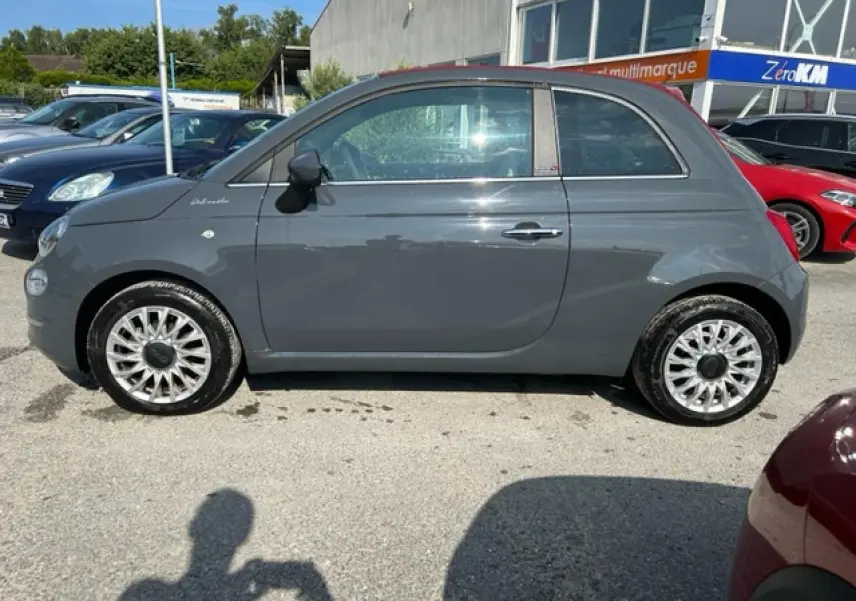 Vue de profil côté gauche d'une FIAT 500C cabriolet 2021 gris avec capote rouge fermée et jantes argentées.