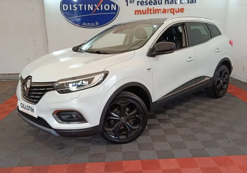 Renault Kadjar blanc vue 3/4 avant droit, jantes noires brillantes et phares LED allumés en intérieur showroom.