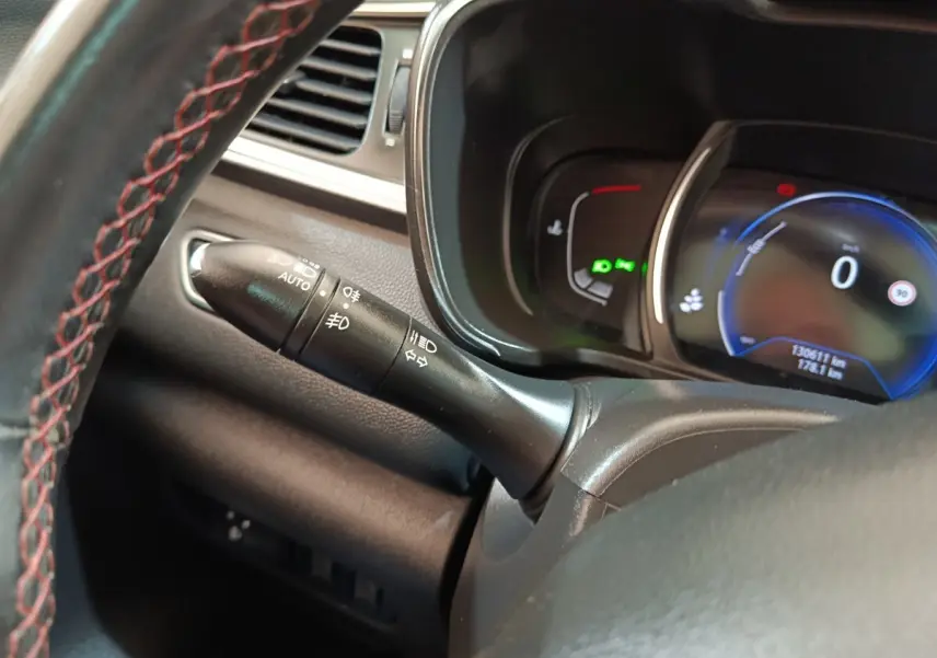 Gros plan sur la manette de phares et clignotants à gauche du volant cuir du Renault Kadjar blanc, tableau de bord digital visible.