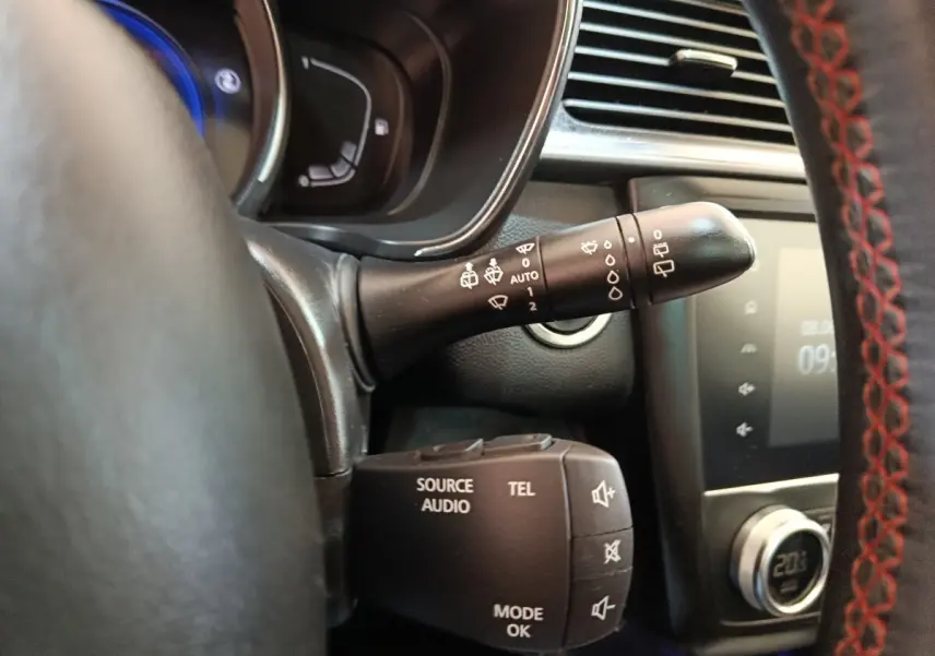 Gros plan intérieur sur commandes au volant du Renault Kadjar blanc, avec volant cuir noir et surpiqûres rouges visibles.