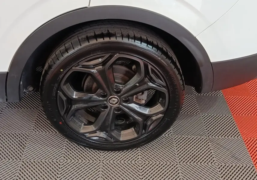 Gros plan sur la roue arrière droite noire brillante d’un Renault Kadjar blanc, avec logo Renault au centre.
