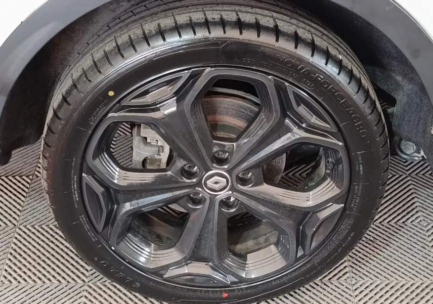 Gros plan sur la roue arrière droite noire d’un Renault Kadjar blanc, avec jante et pneu visibles sur sol texturé.