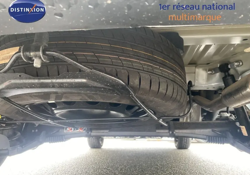 Vue en contre-plongée sous le Citroën Berlingo Fourgon blanc, montrant la roue de secours et le système de suspension arrière.