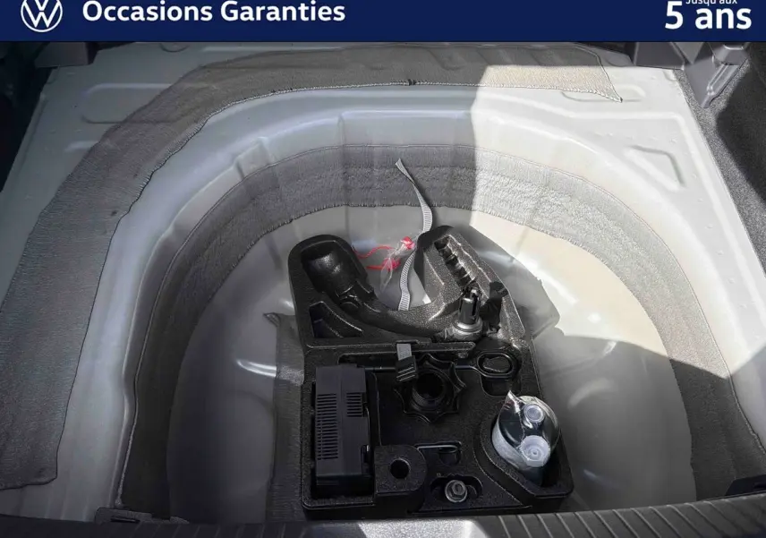 Vue plongeante sur le coffre ouvert d’un Volkswagen Taigo gris, montrant le rangement sous plancher avec attelage amovible.