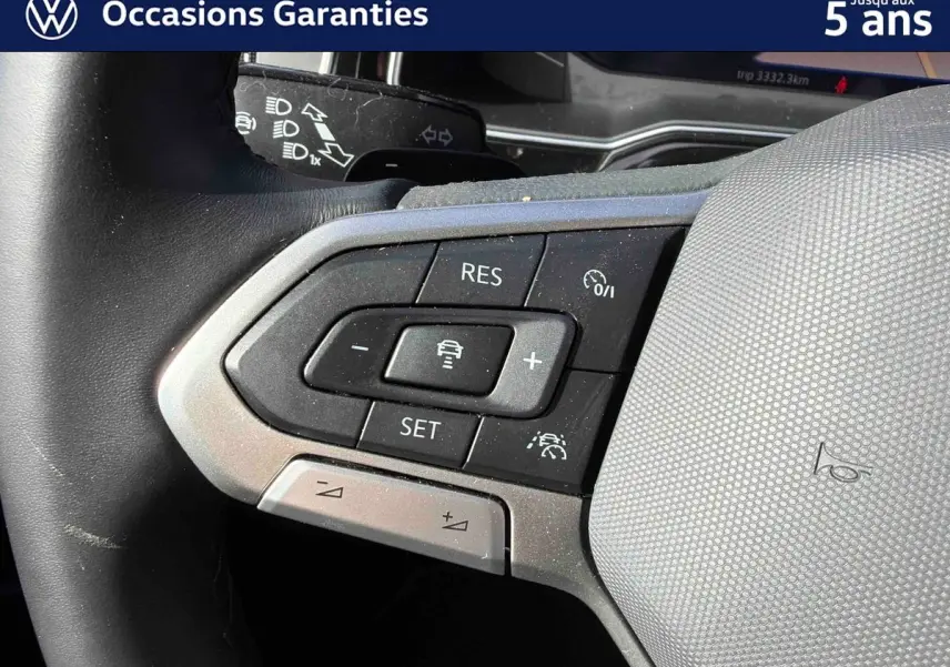 Gros plan sur les commandes du volant gris du Volkswagen Taigo 2025, avec boutons de régulateur de vitesse et assistance conduite.