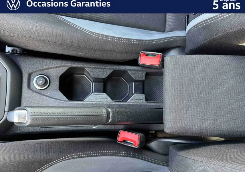 Vue plongeante sur la console centrale intérieure du Volkswagen Taigo 2025, avec frein à main manuel et sièges gris.