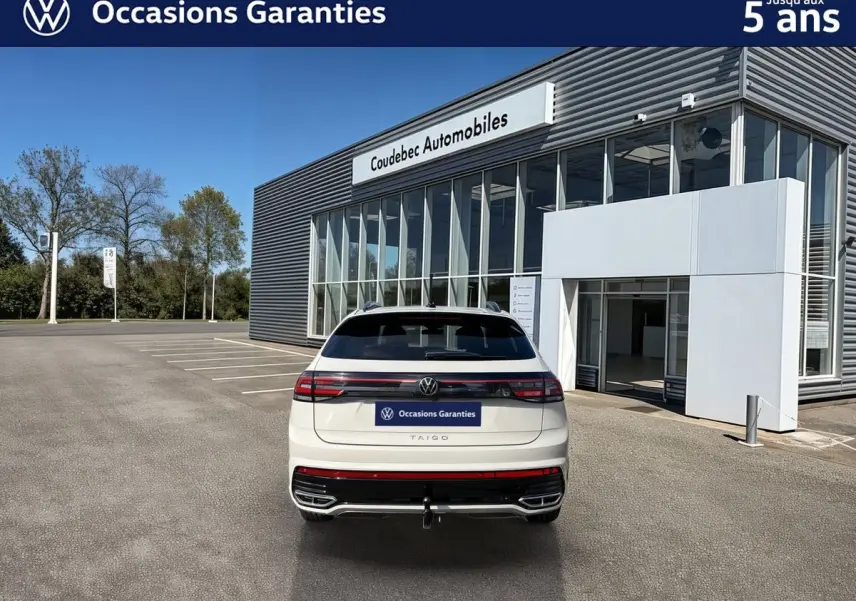Vue arrière d'un Volkswagen Taigo gris clair avec attelage amovible, stationné devant un concessionnaire.