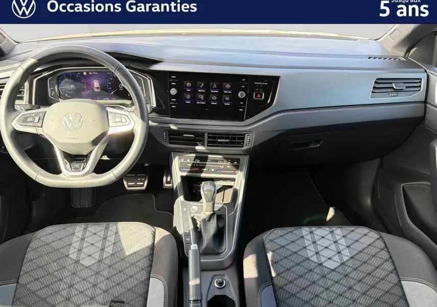 Vue intérieure avant du Volkswagen Taigo 2025, montrant le volant multifonctions, la console centrale et les sièges tissu gris à motifs.
