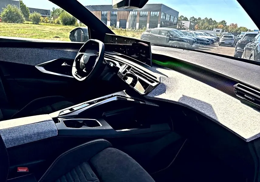 Vue intérieure côté conducteur du Peugeot 5008 Hybrid 145 GT 2025, tableau de bord clair avec écran tactile et volant multifonction.