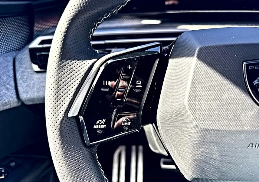 Gros plan sur le volant cuir perforé côté gauche du Peugeot 5008 Hybrid 145 GT 2025 avec commandes multifonctions.