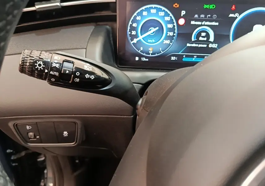 Gros plan sur le commodo des phares et clignotants à gauche du volant d’un Hyundai Tucson 2021, tableau de bord digital visible.