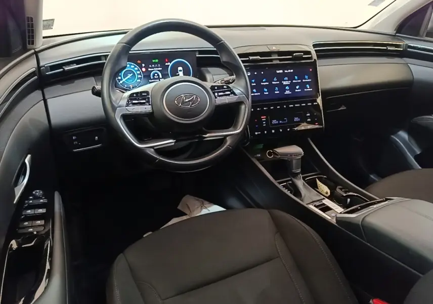 Vue intérieure avant du Hyundai Tucson 2021, tableau de bord noir avec écran tactile et volant multifonctions.
